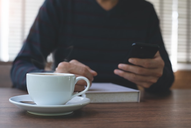 Mann mit Handy und Lesebuch im Café