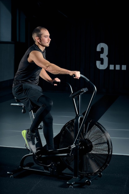 Mann mit Heimtrainer im Fitnessstudio. Fitness-Mann mit Air-Bike für Cardio-Training im Functional Training Gym.