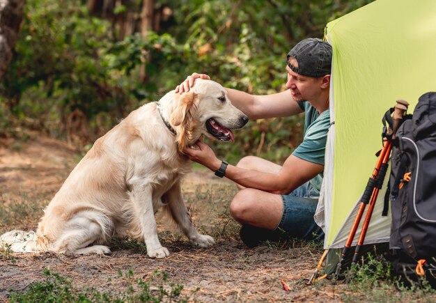 Mann mit Hund, der neben Zelt in der Natur sitzt