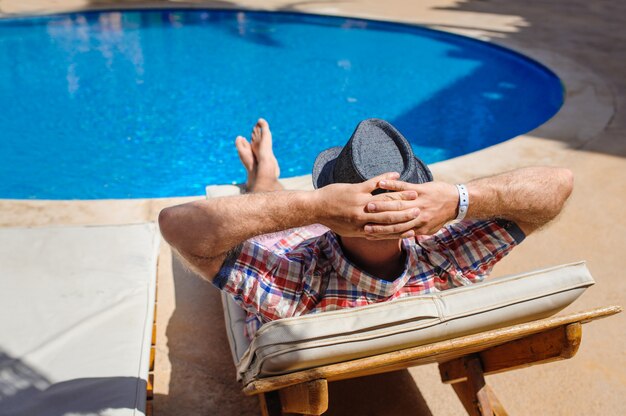 Mann mit Hut beim Sonnenbaden auf einer Sonnenliege am Pool