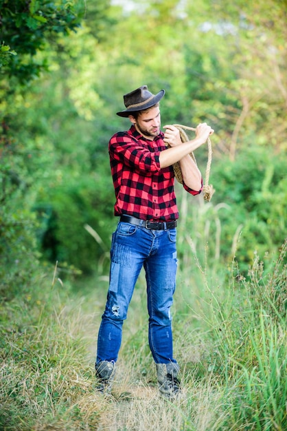 Mann mit Hut halten Seil Ranch Berufe Lasso-Tool Amerikanischer Cowboy Lasso gebunden eingewickelt Westliches Leben Mann Cowboy Natur Hintergrund Ranchbesitzer Sattle Zuchtkonzept Cowboy auf dem Land