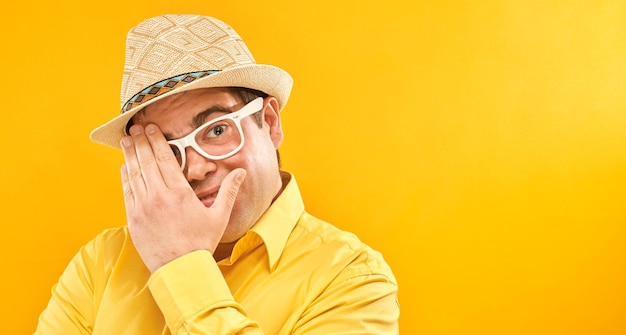 Mann mit Hut und Brille, der durch die Finger guckt, die die Augen mit Handflächen bedecken, die auf gelbem Hintergrund isoliert sind Phobienkonzept