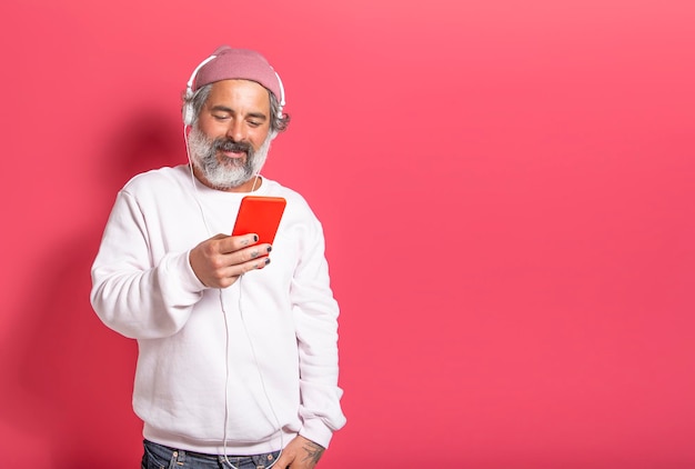 Mann mit Hut und weißem Bart, der Streaming-Musik mit Kopfhörern hört, isoliert auf pinkfarbenem Studiohintergrund mit Platz für Text