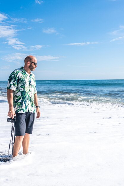 Mann mit Kamera geht am Strand entlang