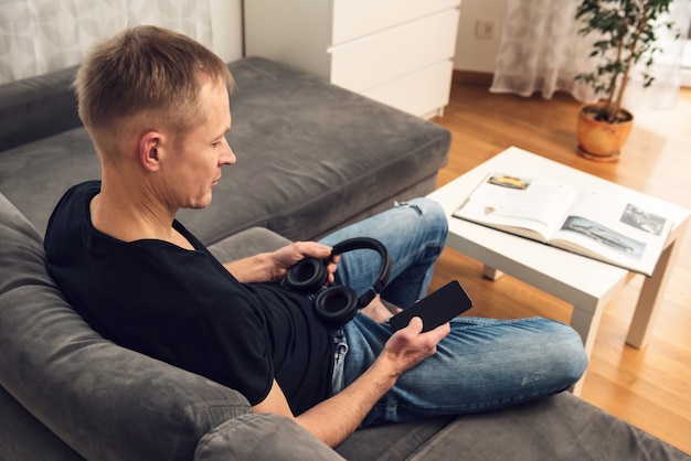 Mann mit Kopfhörer und mit Smartphone sitzt auf der Couch