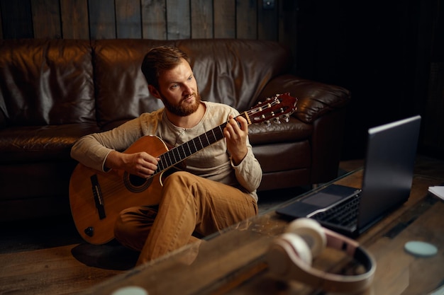 Mann mit Kopfhörern, die Gitarre spielen und auf den Laptop-Bildschirm schauen. Online-Musikunterricht