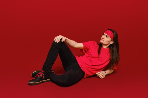 Mann mit langen Haaren sitzt im roten Studio auf dem Boden