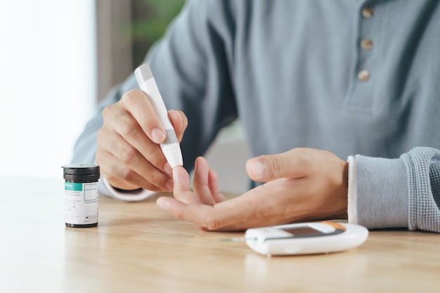 Mann mit Lanzette am Finger zur Überprüfung des Blutzuckerspiegels durch Glukosemeter, Diabeteskonzept