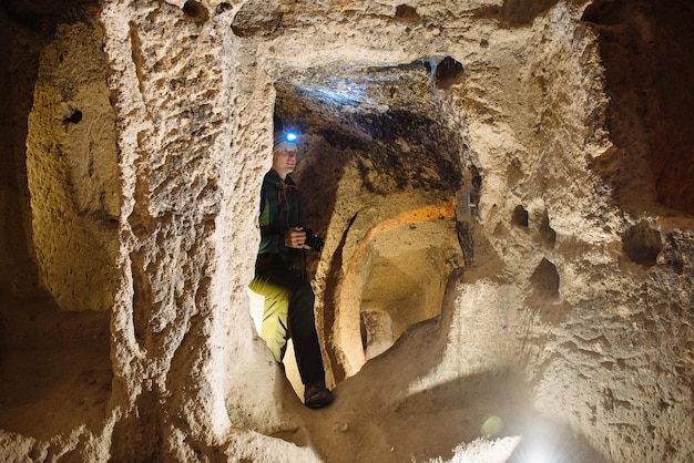 Mann mit Lichter erkunden Höhlen in Derinkuyu alten mehrstöckigen unterirdischen Stadt, in der Provinz Nevsehir, Kappadokien, Türkei. Innenraum des felsigen Raumes.