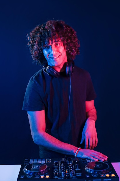 Mann mit lockigem Haar, der DJ-Equipment verwendet und im dunklen, neonbeleuchteten Raum steht