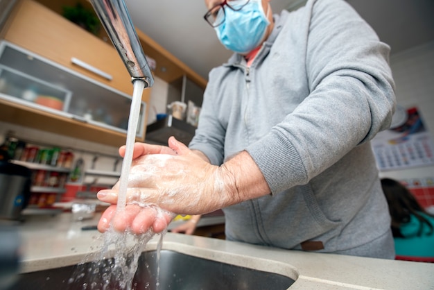 Mann mit Maske wäscht Hände zur Vorbeugung gegen Covid-19