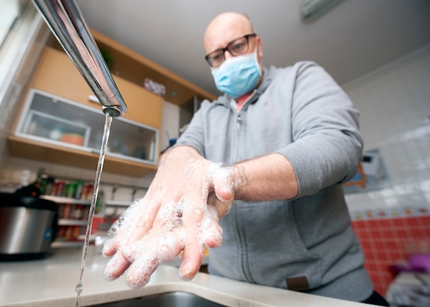 Mann mit Maske wäscht Hände zur Vorbeugung gegen Covid-19