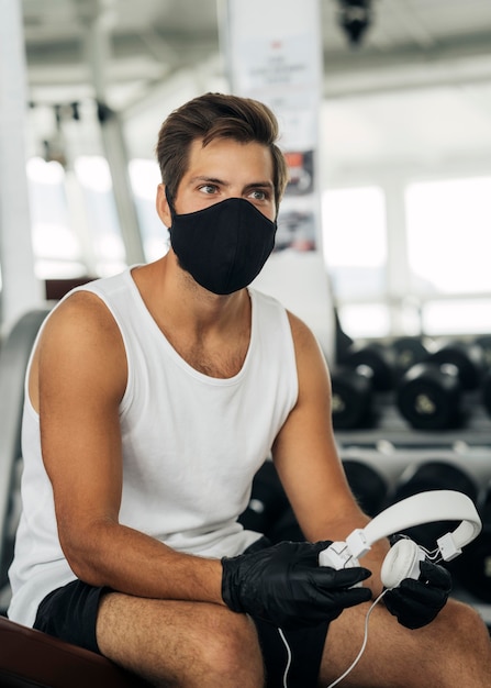 Foto mann mit medizinischer maske und kopfhörern im fitnessstudio