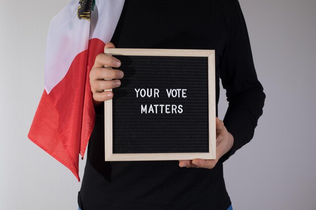 Mann mit mexikanischer Flagge, der ein Briefbrett mit dem Text Your Vote Matters auf weißem Hintergrund hält