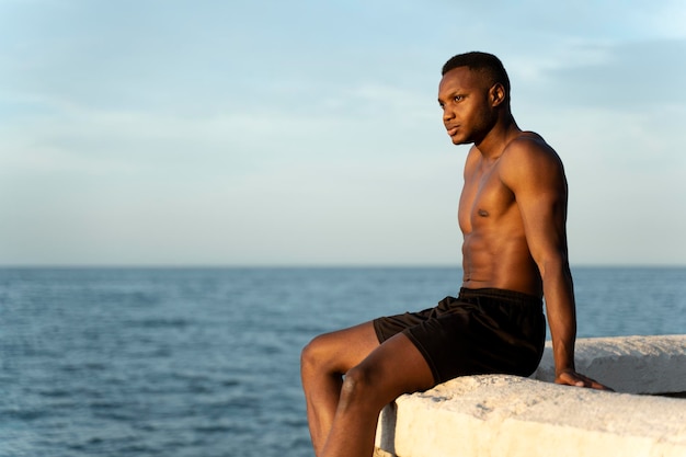 Mann mit nacktem Oberkörper, der am Strand steht und wegschaut, während er sich in der Sonne erwärmt