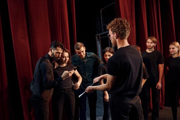 Foto mann mit notizblock übt seine rolle gruppe von schauspielern in dunkler kleidung bei der probe im theater