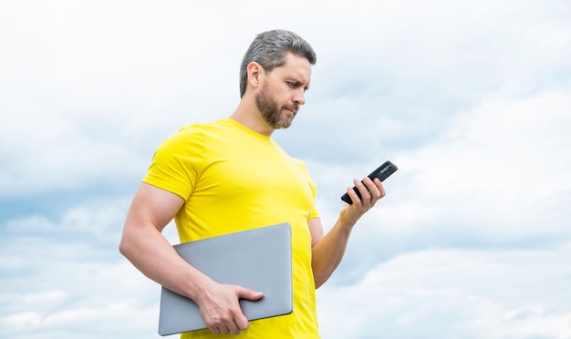 Mann mit PC im Chat auf Smartphone auf Himmelshintergrund