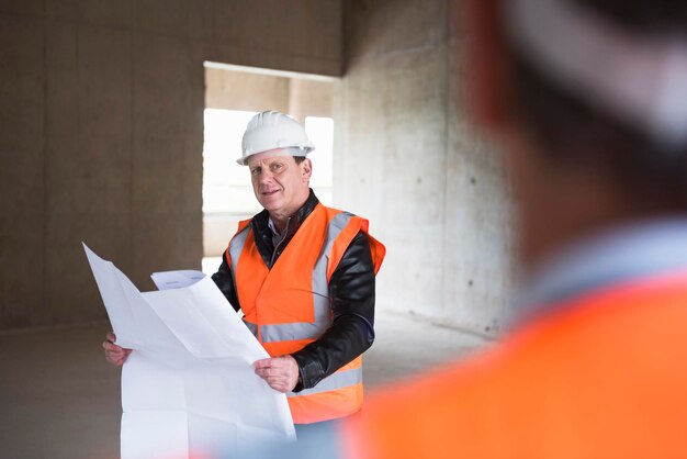 Mann mit Plan mit Warnweste im Gebäude im Bau