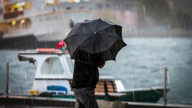 Mann mit Regenschirm am Meer an einem regnerischen Tag