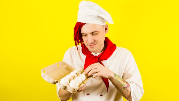 Mann mit roten Dreadlocks hält es in seiner Hand Hühnereier Selbstbewusster junger Koch in weißem Hemd und roter Krawatte mit Hühnereiern