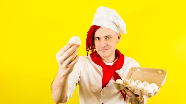 Mann mit roten Dreadlocks hält es in seiner Hand Hühnereier Selbstbewusster junger Koch in weißem Hemd und roter Krawatte mit Hühnereiern