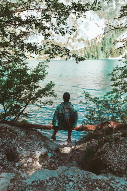 Mann mit Rucksack, der am Holzstamm sitzt und das Wanderkonzept mit Blick auf das Wasser genießt