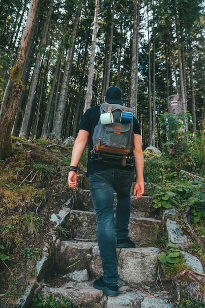 Mann mit Rucksack, der über eine Steintreppe geht, die zum Wald führt