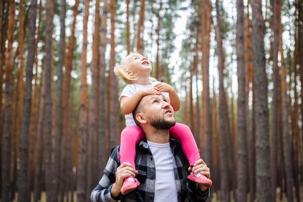 Mann mit Rucksack trägt ein Kind auf den Schultern im Wald Familienwanderung in die Berge oder in den Wald