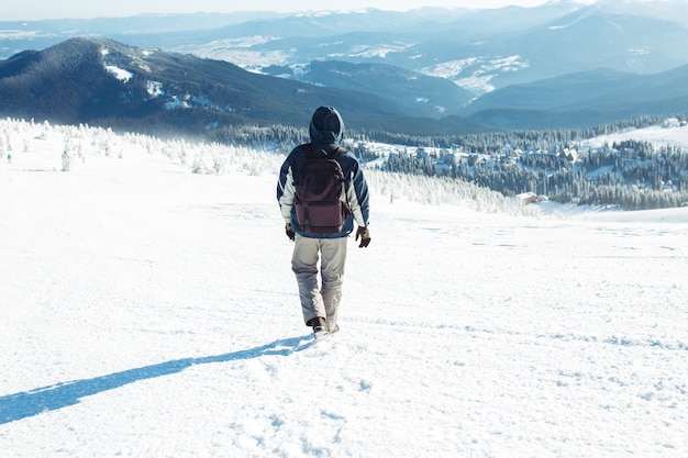 Mann mit Rucksack Trekking in den Bergen. Kaltes Wetter, Schnee auf Hügeln. Winterwandern. Der Winter kommt, erster Schneefall. Konzept von Reisen, Ruhe, Entspannung