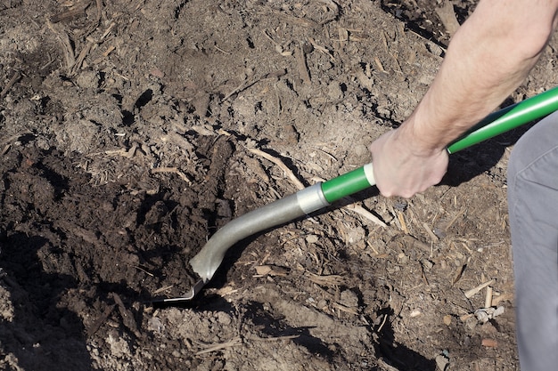 Mann mit Schaufel gräbt Schmutz im Gartenbett