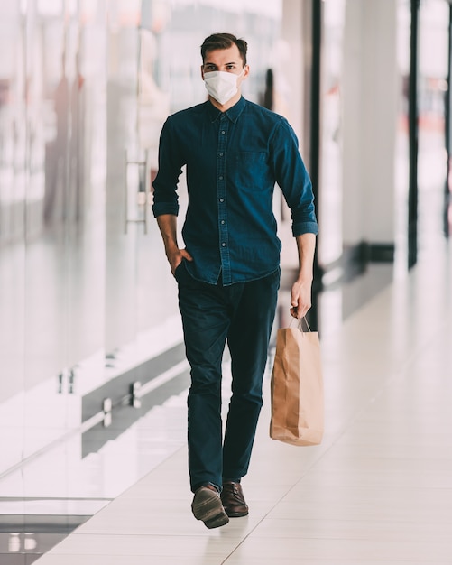 Mann mit Schutzmaske, der in der Nähe eines Supermarkts vorbeigeht. Konzept des Gesundheitsschutzes.