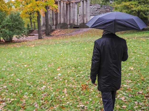 Mann mit schwarzem Regenschirm im Park.