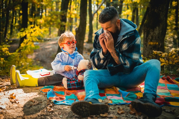 Mann mit Serviette niesen im gelben Park Papa und Sohn spielen zusammen Papa und Sohn in Pullovern in ...