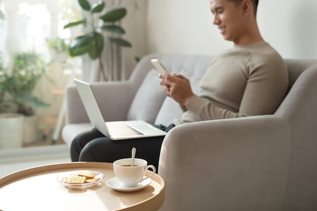 Mann mit Smartphone und Laptop auf dem Sofa