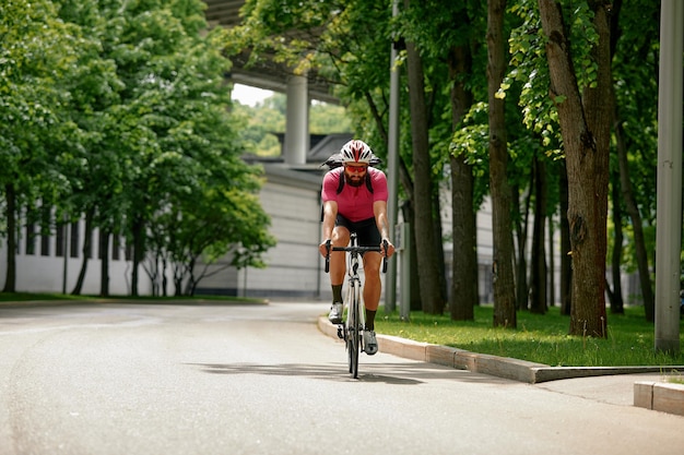 Mann mit Sonnenbrille beschleunigt auf der Straße vor dem Hintergrund des Sommerparks Mann mit einem Fahrrad-Hobby fährt im Park