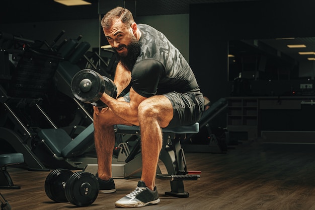 Mann mit Sportkörper, der Hanteln an der Turnhalle hebt