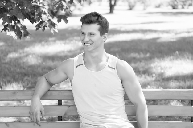 Mann mit starken Händen Bizeps Trizeps an einem sonnigen Sommertag Glücklicher Sportler, der draußen auf der Naturlandschaft sitzt Sportler, der auf einer Holzbank im Park lächelt Gesundes Lebensstilkonzept