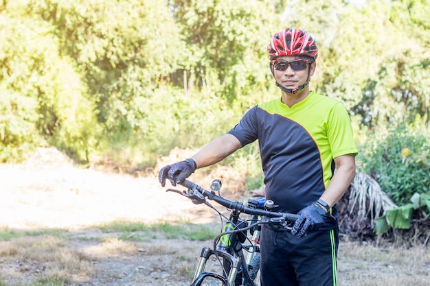 Mann mit Sturzhelmhandschuh zur Sicherheit Fahrradfahren an der Landschaftsstraße entlang einem Wald