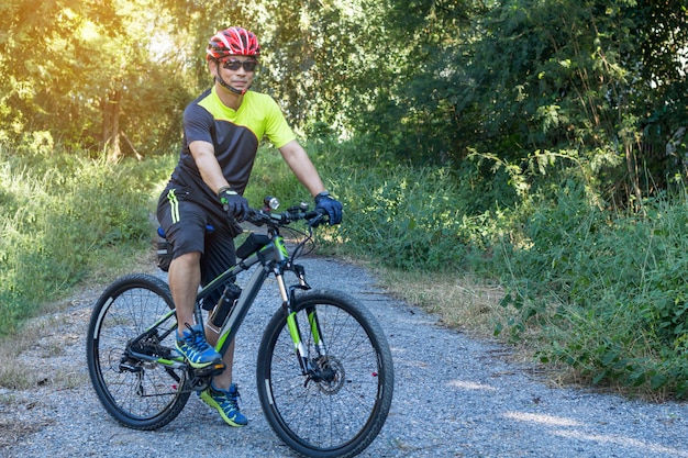 Mann mit Sturzhelmhandschuh zur Sicherheit Fahrradfahren an der Landschaftsstraße entlang einem Wald