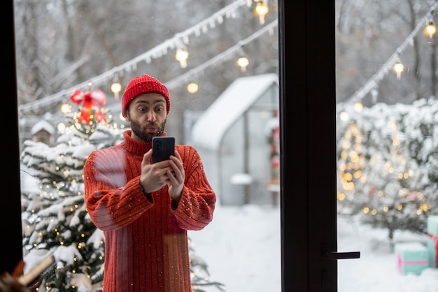 Mann mit Telefon in der Nähe des Weihnachtsbaums im Freien