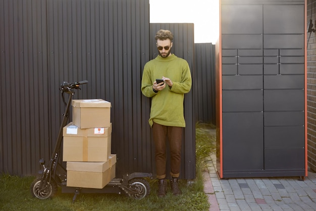 Mann mit Telefon in der Nähe von automatischem Postterminal und Roller