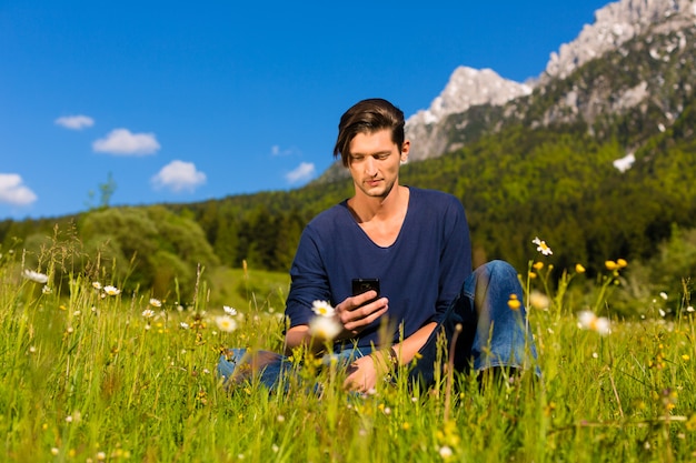 Mann mit Telefon sitzt in den Bergen