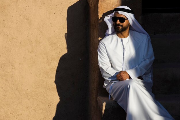 Mann mit traditioneller Kleidung und Sonnenbrille sitzt an der Wand