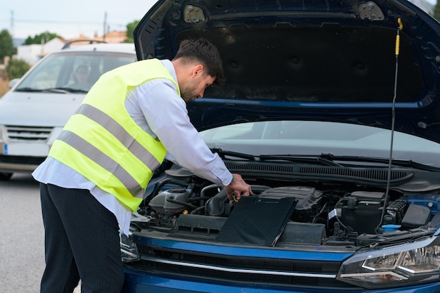 Mann mit Warnweste schaut auf die Motorhaube seines Autos