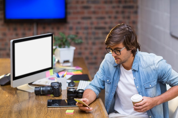 Mann mit Wegwerfbecher mit Handy im Büro