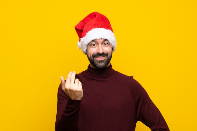 Mann mit Weihnachtshut über der lokalisierten gelben Wand, die einlädt, mit der Hand zu kommen. Schön, dass Sie gekommen sind