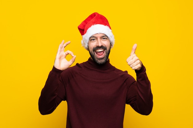 Mann mit Weihnachtshut über der lokalisierten gelben Wand, die okayzeichen und Daumen herauf Geste zeigt