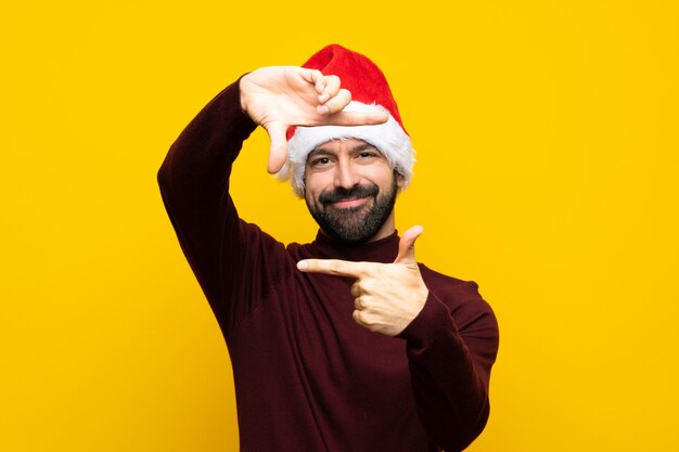 Mann mit Weihnachtshut über lokalisiertem gelbem Wandfokussierungsgesicht. Rahmensymbol