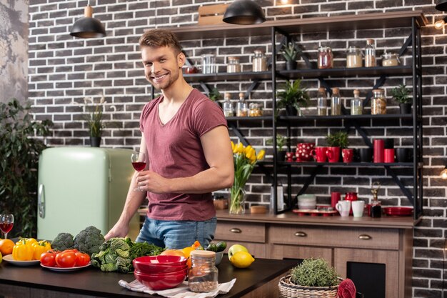 Mann mit Wein. Schöner bärtiger blonder Mann mit Muskeln, der in der Küche steht und Wein trinkt