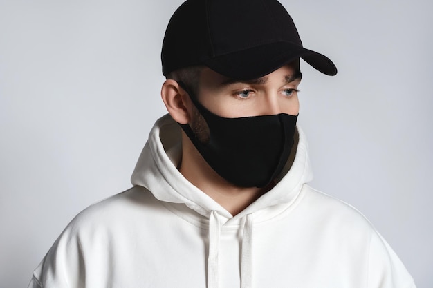 Mann mit weißem Hoodie, schwarzer Baseballkappe und Stoffgesichtsmaske